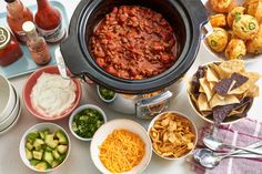 a crock pot filled with chili, cheese and tortilla chips next to other foods