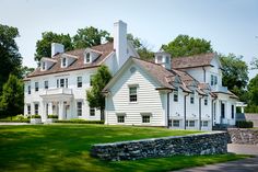 a large white house sitting in the middle of a lush green field next to a stone wall