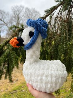 a hand holding a white and blue llama ornament in front of a pine tree