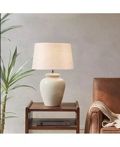 a white lamp sitting on top of a table next to a brown chair and potted plant