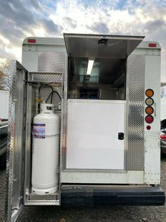 the back end of a white trailer with an open door and water tank in it