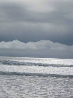 two surfers walking into the ocean with their surfboards under an overcast sky