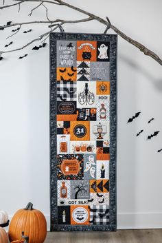 a halloween quilt hanging on the wall next to pumpkins and branches with bats in the background