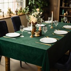 a green table cloth with white plates and wine glasses is set for a formal dinner