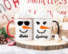 two coffee mugs with snowmen on them sitting next to a teddy bear and christmas decorations