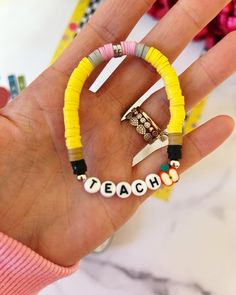 a person's hand holding two bracelets with letters on them that spell out teach