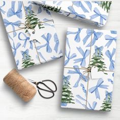 wrapping paper and scissors on a white table with blue christmas tree designs wrapped in twine