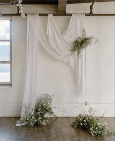 flowers and greenery are arranged on the floor in front of an open white curtain