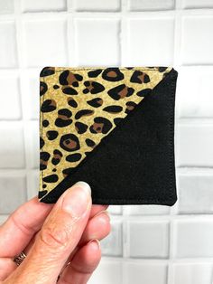 a hand holding up a small wallet with a leopard print on the front and black bottom