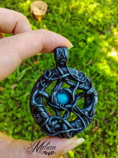 a hand holding a small black pendant with blue glass beads in it's center