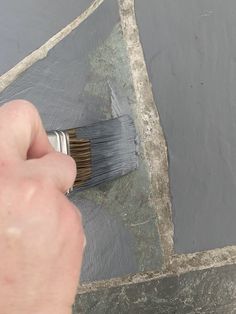 a hand holding a paint brush over a piece of slate that has been stained gray