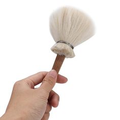 a hand holding a white shaving brush on top of it's head, against a white background