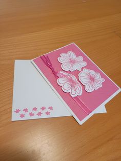 a pink and white greeting card with flowers on the front, sitting on a wooden table