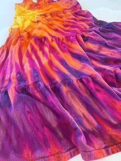 a dress made out of tie dye on a white tablecloth with a pink, orange and yellow design