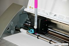 a close up of a machine that is cutting paper with a pink and blue marker