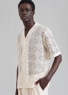 a man standing in front of a gray background wearing a white shirt and beige shorts