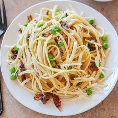 a white plate topped with pasta and peas on top of a table next to a fork