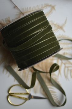 a spool of olive green satin ribbon next to gold scissors and fern leaf decorations