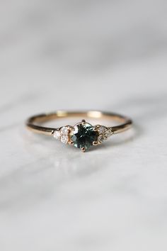 an engagement ring with two diamonds on top and a green stone in the middle, sitting on a marble surface