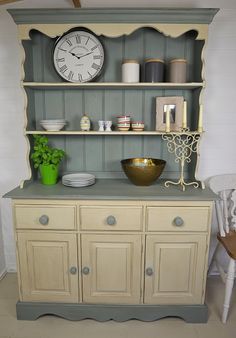 an old china cabinet with a clock on the wall above it and dishes in front of it