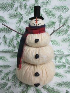 a snowman with a hat and scarf on it's head sitting in front of pine branches