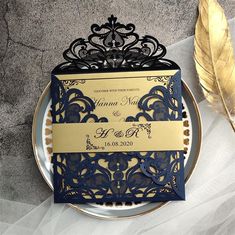 a plate with a gold and blue wedding card on it next to a golden feather