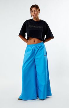 Stay effortlessly cool with these Reebok Angel Wide Leg Track Pants. Crafted from recycled fabric, they feature a low-rise, elastic waistband, side hand pockets, and snap-button details, all complemented by Reebok's soft-touch logo for a relaxed fit with wide-leg openings.13" rise28" inseam40" leg openingsSolid color track pantsLow-riseElastic waistbandSide hand pocketsSnap-button side detailsReebok soft-touch logoWide leg openingsRelaxed fit100% recycled polyesterMachine washableModel is wearing a size smallModel measurements: 5’9” height, 32” bust, 25” waist, 34” hipsMeasurements taken from a size smallLearn more about PacSun eco items Reebok Womens Angel Wide Leg Track Pants - Blue size Small Blue Sportswear Bottoms With Elastic Side Panels, Blue Sportswear Bottoms With Ribbed Waistband, Sporty Spring Bottoms With Elastic Side Panels, Blue Relaxed Fit Pants With Ribbed Waistband, Blue Nylon Workout Pants, Sports Wide Leg Bottoms With Elastic Side Panels, Sports Wide-leg Bottoms With Elastic Side Panels, Streetwear Wide Leg Bottoms With Elastic Side Panels, Blue Workout Bottoms With Elastic Side Panels