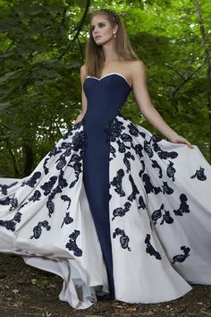 a woman in a blue and white gown standing on the ground with trees behind her