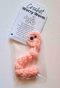 a pink crochet wormy worm on a white surface next to a card