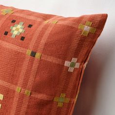 an orange pillow with yellow and green squares on the front, sitting against a white wall