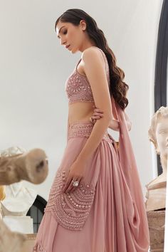 Blush pink pre-draped, lehenga saree with scallop detailing and highlighted with pearls, crystal embroidery. Paired with a padded blouse with all over sequins, thread, pearls and crystal work.
Components: 2
Pattern: Embroidery, Embellished
Type Of Work: Scallop, Thread, Beads, Sequins, Pearl, Crystal
Neckline: Scoop Neck
Sleeve Type: Sleeveless
Fabric: Flat Chiffon and Organza
Color: Pink
Other Details: 
Model height: 5 ft 7 inches, wearing size XS
Blouse:
Padded

Occasion: Destination Wedding - Traditional Draped Lehenga With Mirror Work, Semi-stitched Draped Sets With Mirror Work, Elegant Draped Choli For Eid, Draped Lehenga With Mirror Work In Georgette, Semi-stitched Silk Draped Lehenga, Georgette Draped Traditional Wear For Wedding, Draped Georgette Traditional Wear For Wedding, Bollywood Style Semi-stitched Draped Sets, Draped Choli For Eid Party