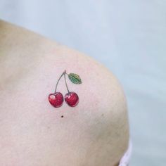 a small cherry tattoo on the back of a woman's left shoulder, with two cherries attached to it