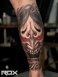 a man's leg with a tattoo on it that has a demon face and red eyes