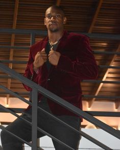 a man in a red jacket and black pants is standing on the stairs with his tie around his neck