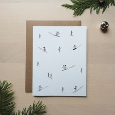 a greeting card with trees and skis on it next to a christmas tree ornament