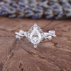 an engagement ring with a pear shaped diamond center surrounded by small white diamonds on a piece of wood