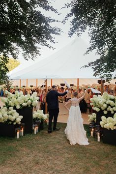 a bride and groom walking down the aisle at their outdoor wedding in front of a tent