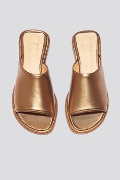 The Pileta slide is a streamlined version of the Pileta Sport Slide, featuring a sleek leather sole. The absence of details creates the perfect canvas for metallic bronze kidskin to shine. Slipping into a simple flat sandal in a striking material can be the answer to "dressing up" on a summer night when paired with a long strappy dress. Who it’s for: The woman who likes being the most comfortable person at the party.Kidskin upper with vegetable tanned leather lining and a 25 mm stacked leather h Metallic Open Toe Mules For Summer, Classic Gold Sandals For Summer, Classic Gold Sandals With Leather Footbed, Gold Leather Sandals With Rubber Sole, Metallic Open Toe Slides, Sleek Metallic Sandals For Summer, Gold Leather Footbed Slides, Gold Slides With Leather Footbed, Sleek Gold Leather Sandals