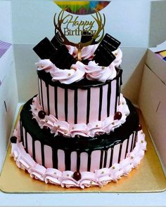 a three tiered cake with pink and black frosting on top in a box