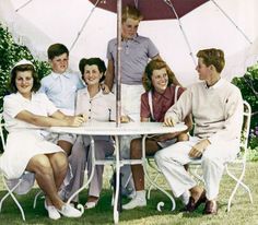 a group of people sitting around a table with an umbrella over it's head