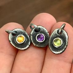 three different colored stones are in the middle of a handmade pendant on a person's finger