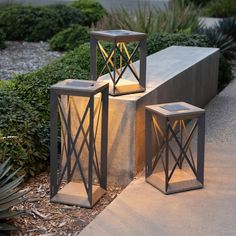 two lanterns sitting next to each other on top of a cement block in the middle of a garden