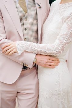 the bride and groom are dressed in pastel colored suits with lace sleeves on their arms