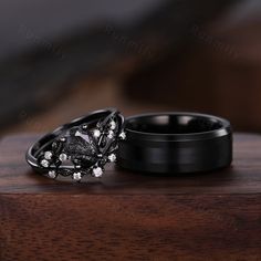 two black wedding rings sitting on top of each other with white flowers in the middle