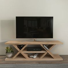 a flat screen tv sitting on top of a wooden stand next to a potted plant