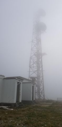 a tall tower sitting on top of a lush green field next to a building in the fog