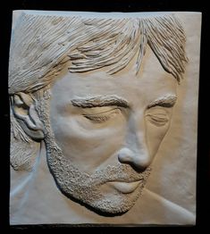 a clay sculpture of a man's face with his eyes closed and hair pulled back