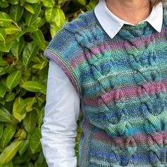 a woman standing in front of some bushes wearing a colorful sweater and vest with buttons on it