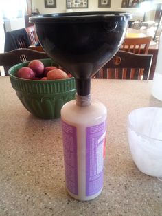 a bottle of liquid sitting on top of a counter next to a bowl of fruit