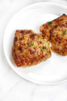 two pieces of chicken sitting on top of a white plate with green garnish